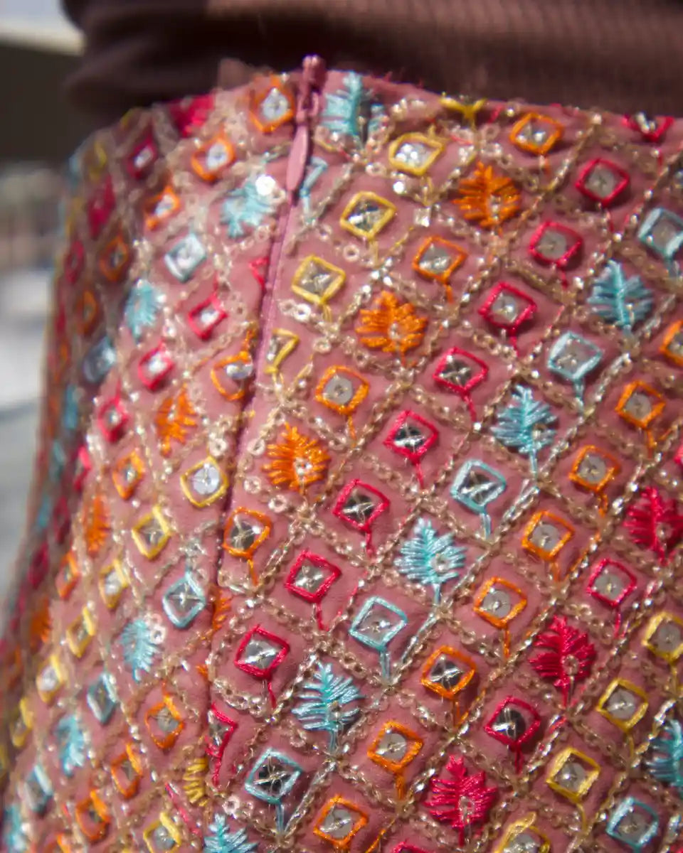 Close-up of colourful thread embroidery and sequin work on a pink mini skirt and closeup of closure of skirt with shown zipper