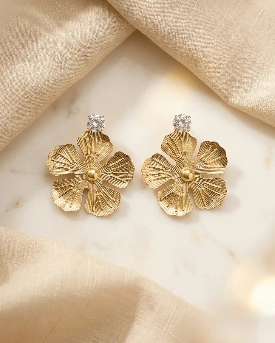Show casing golden coloured metal flower shape earrings with tetured on it , a diamond on top part of earrings