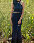 Model wearing black co-odd set with long skirt bottom and crop top with one shoulder pattern and neck tie