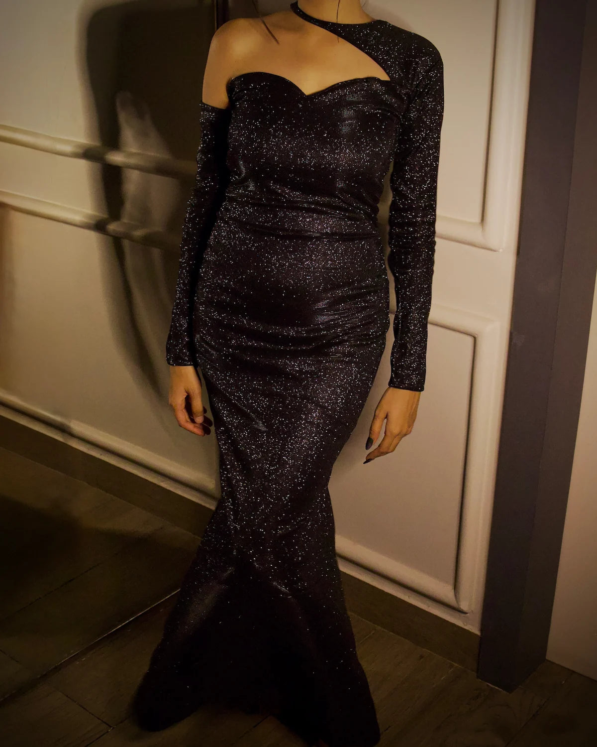 A woman wearing a sparkling black off-the-shoulder evening gown with long sleeves and a fitted mermaid silhouette, a glitter evening long dress