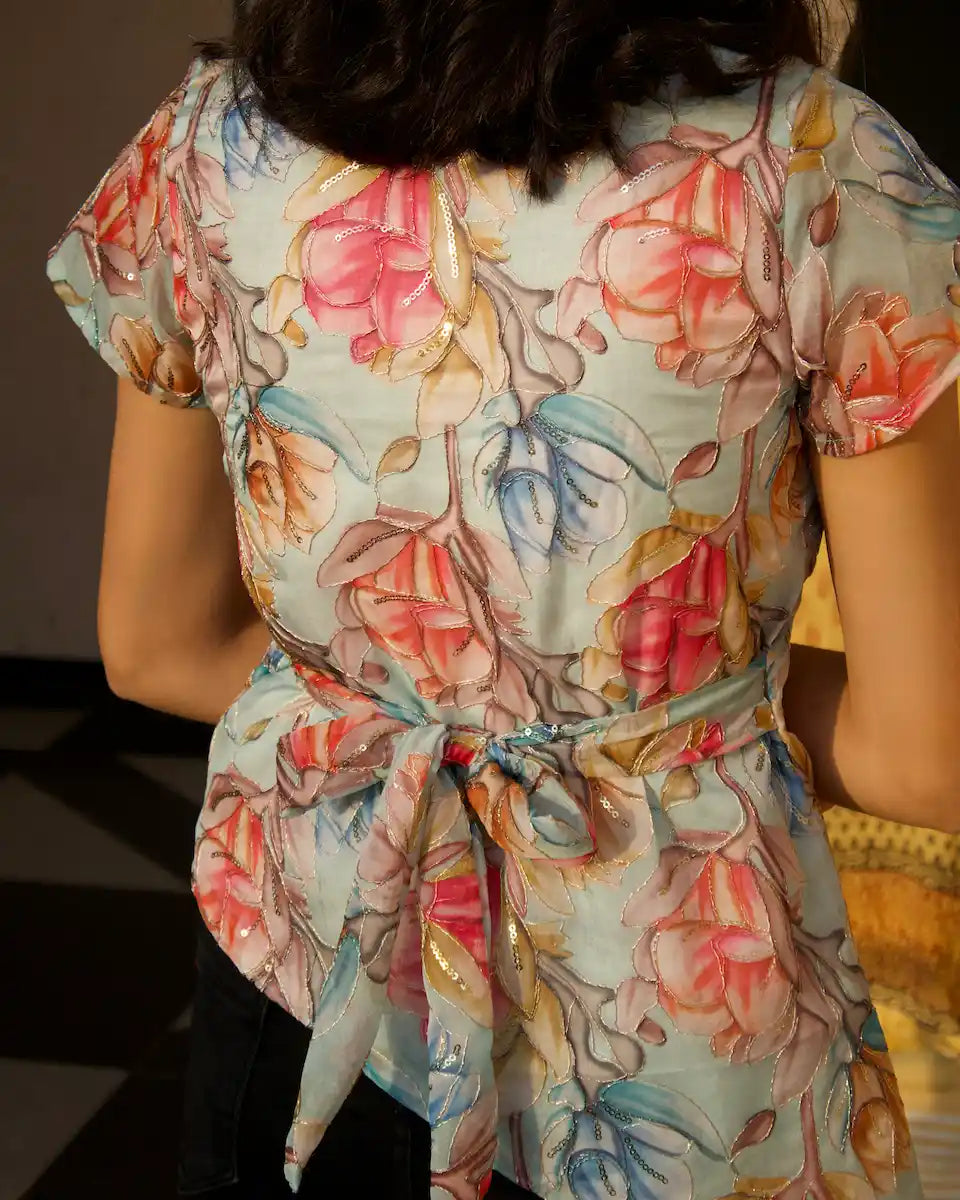 Back view of pastel blue floral top with waist tie bow and sequin outline embroidery