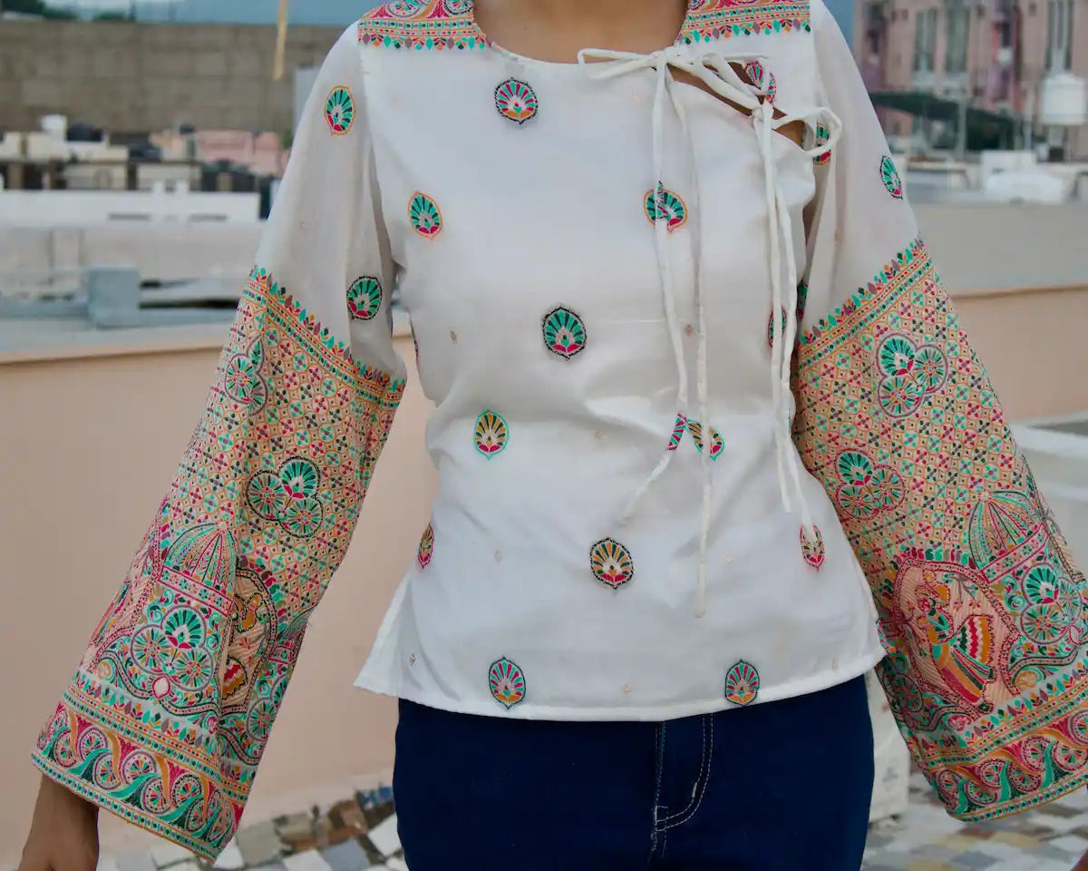 White bell sleeve top with side tie neckline and colourful woven sleeves, styled with dark jeans