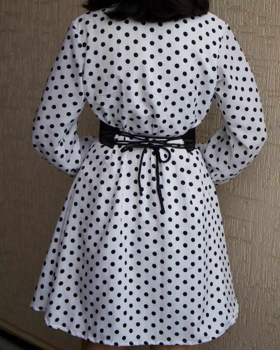 A white bell-sleeve dress with black polka dots, featuring a black corset belt at the waist, shown from the back of dress 